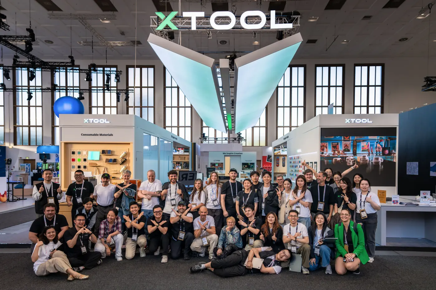 Gruppenaufnahme des xTool Messeteams auf der IFA 2026 in Berlin: etwa vierzig Personen in zwei Reihen vor dem Messestand, darüber das beleuchtete xTool Logo und ein trichterförmiger Deckenaufbau, links und rechts Vitrinen mit Materialproben.