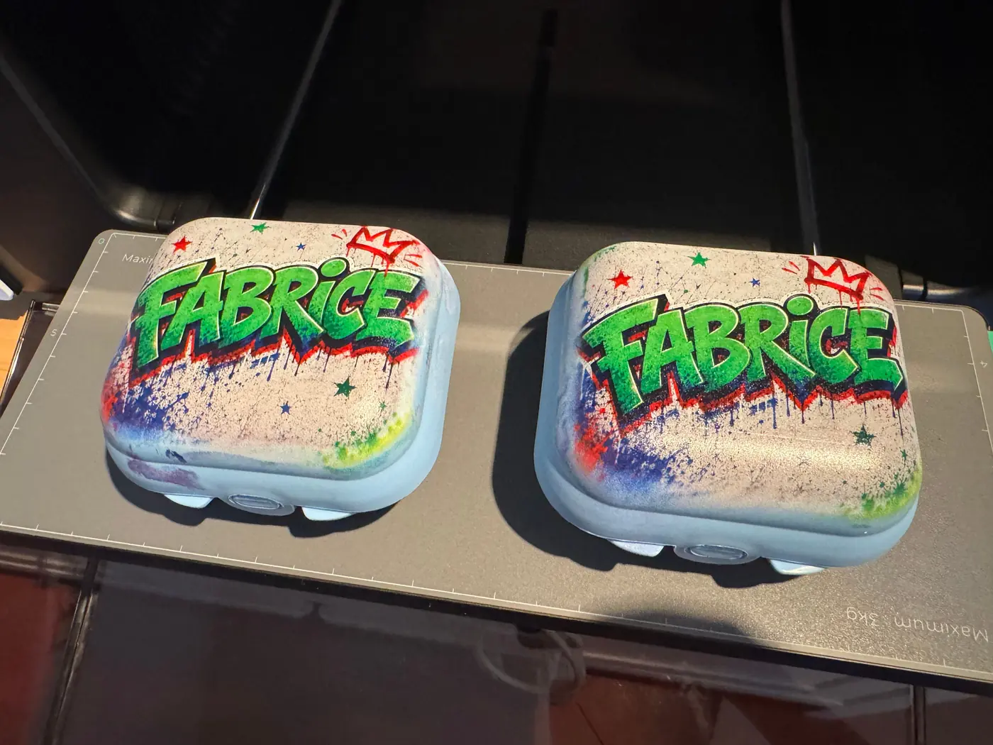 Two pale blue plastic lunch boxes side by side on the base plate of the xTool O1 Omni, both printed on the lid with the same graffiti lettering “Fabrice”.