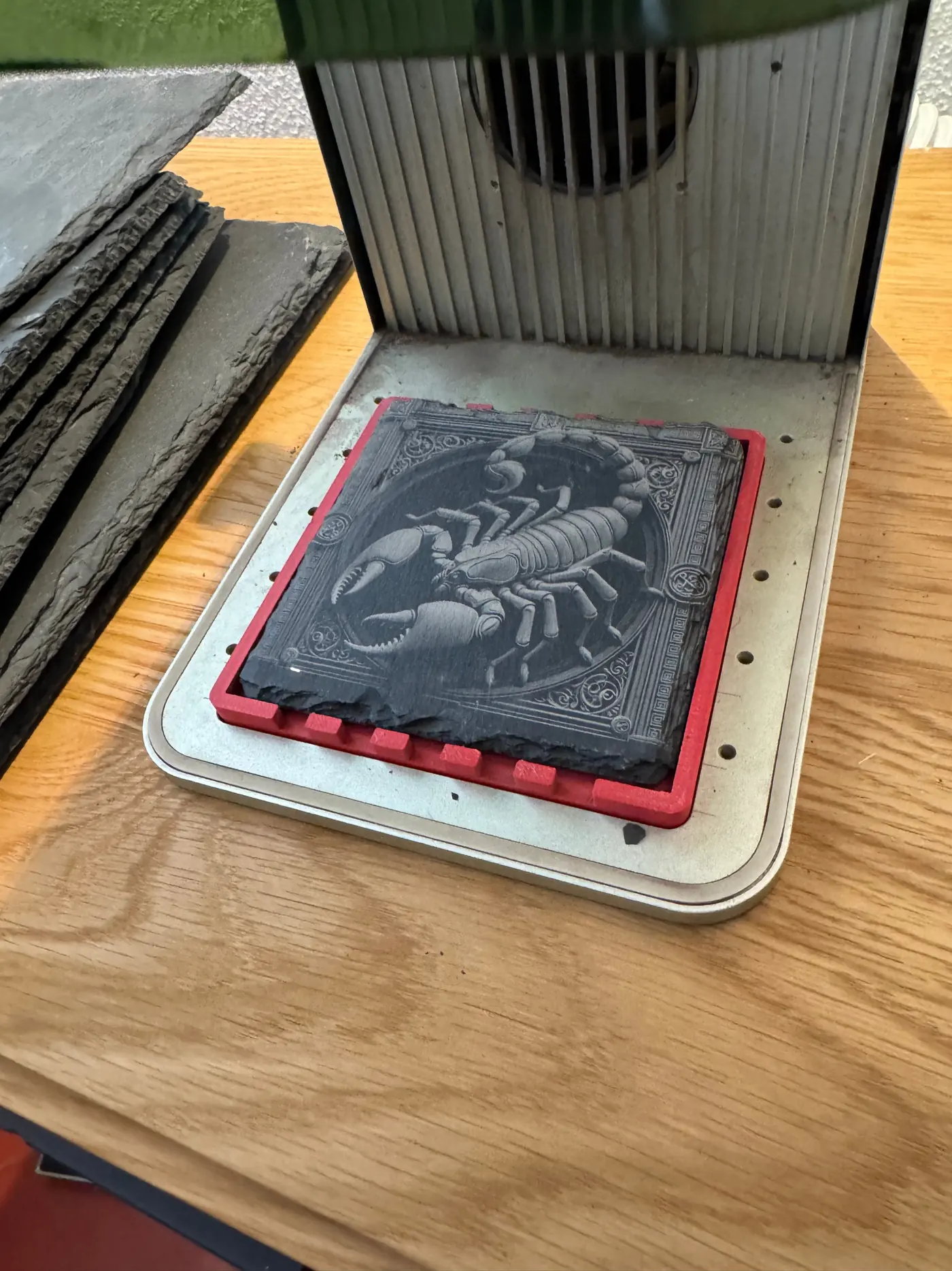 Close view of the engraving: a scorpion in an ornamental frame, light against dark slate.