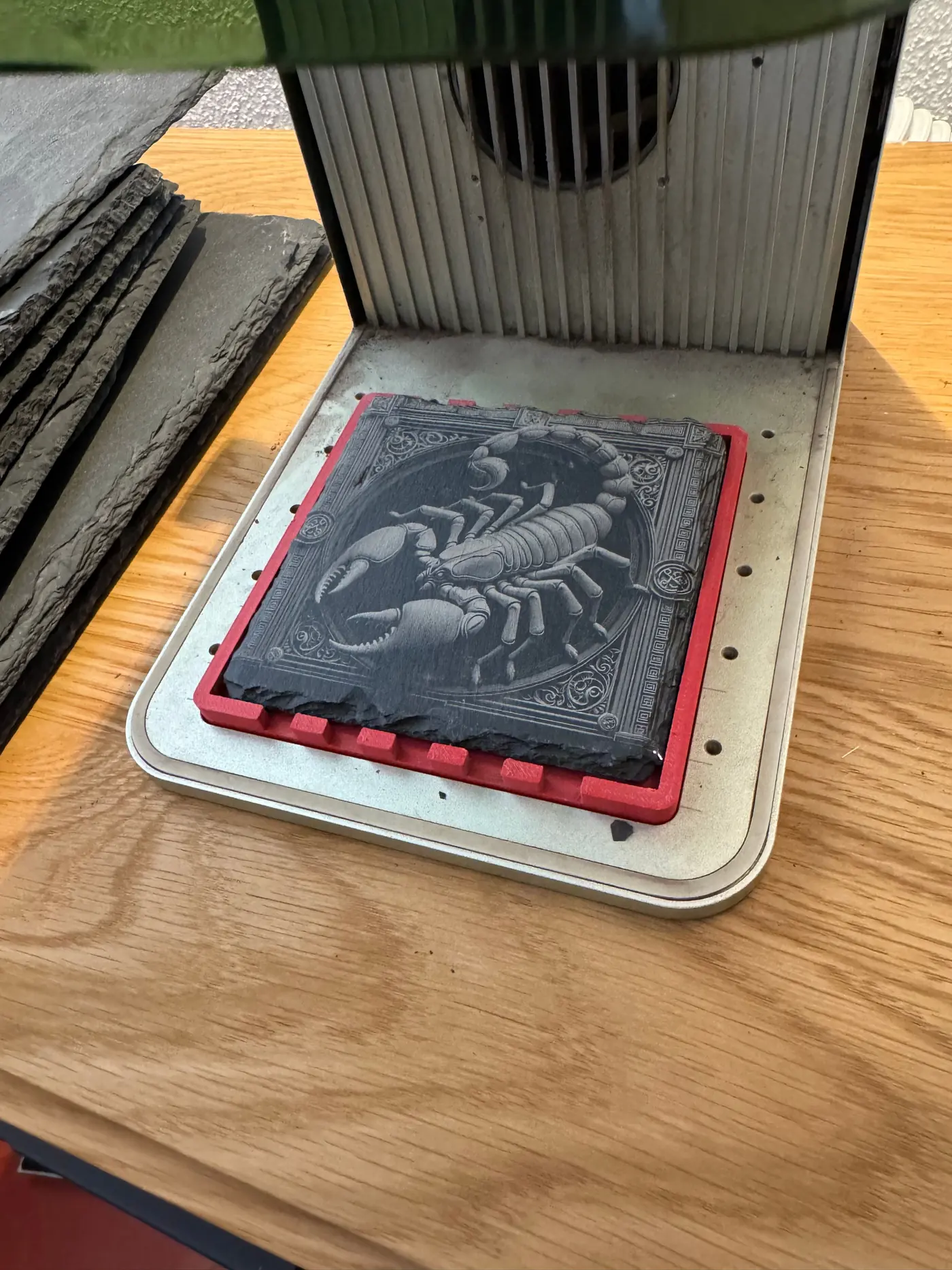 The same slate tile after the run, under the xTool F1: a scorpion engraved inside an ornamental frame.