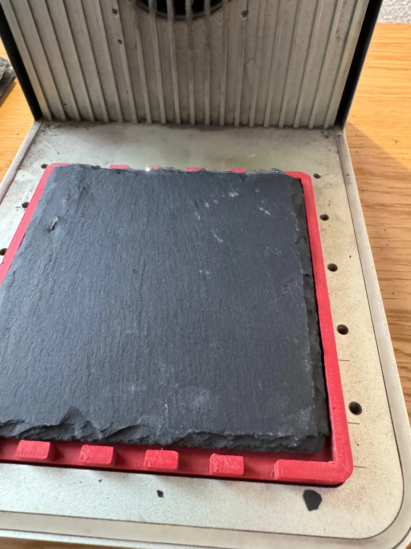 An untouched grey slate tile sits in a red jig on the base plate of the xTool F1.