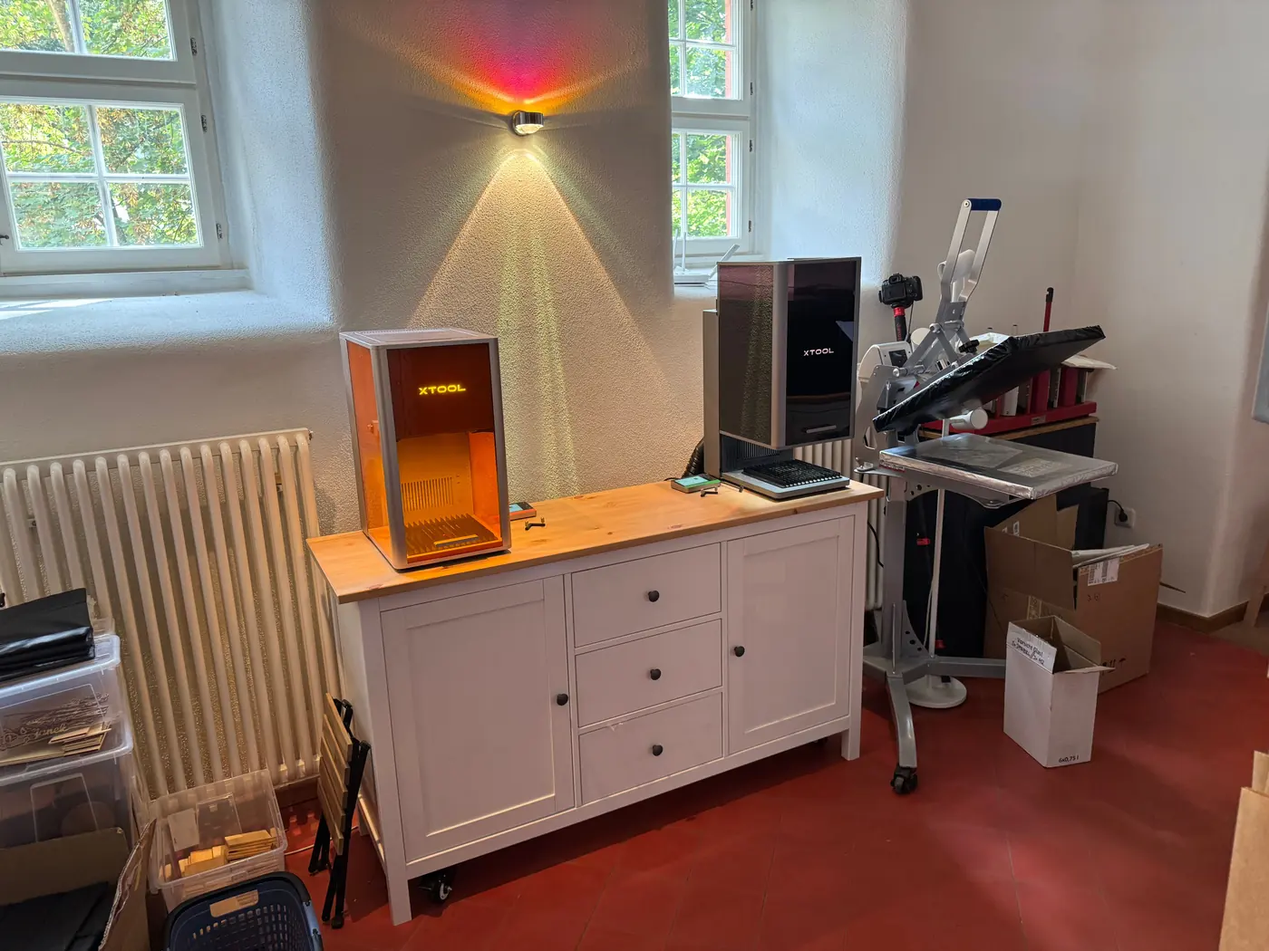 Wide view of the demo spot in Gedern: xTool F2 Ultra UV and F2 Ultra on a light sideboard between two windows, a heat press on the right.