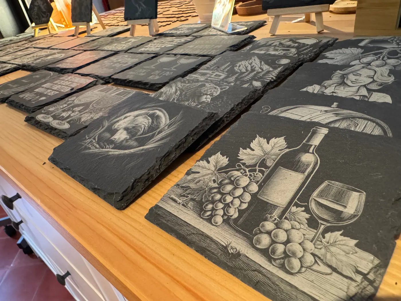 The display in the Regionalladen Gedern: dozens of engraved slate tiles and coasters on a wooden counter, a wine bottle, glass and grapes motif at the front.
